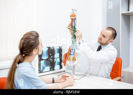 Junge Frau bei der medizinischen Beratung mit erfahrenen Therapeuten zeigen Wirbelsäule Modell im Büro Stockfoto