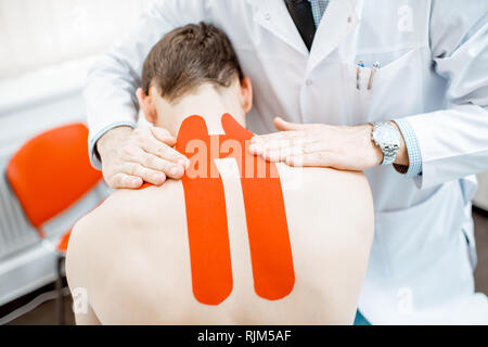 Leitender therapeut Anwendung kinesio Tape auf dem Hals des Mannes während der medizinischen Behandlung im Büro Stockfoto