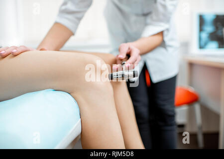 Junge Frau während der medizinischen Untersuchung mit Neurologen testen Reflexe im Büro Stockfoto