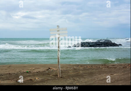 Ein leeres Zeichen vor dem Meer in Fiumicino (Rom). Meer Wellen Felsen stoßen. Strand schießen in einem Winter windigen Tag. Stockfoto