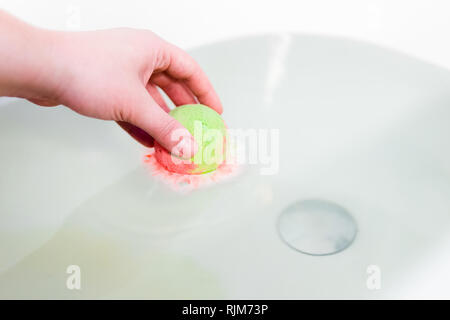 Grüne und rote brodelnde Ball von Badesalz in Händen. Bombe für die Badewanne. Es löst sich in den Händen Stockfoto