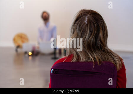 Frau hören crystal Bowls. Frau von hinten zu sehen, hören von einem Mann in Weiß gekleidet Spielen crystal Bowls und Singen im verschwommenen Hintergrund Stockfoto