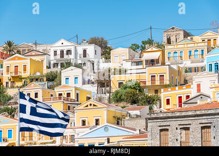 Griechische Flagge und bunten neoklassischen Häuser in der Hafenstadt Symi (Insel Symi, Griechenland) Stockfoto