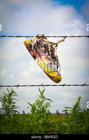 Ein Über-lackiert athletischer Schuh hängt von einem Stacheldrahtzaun vor der Cadillacs Hälfte - im Abstand begraben, bei Cadillac Ranch, in der Nähe von Amarillo, TX Stockfoto