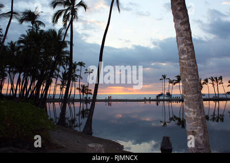 Palmen und den Sonnenuntergang in einem See von Anaehoomalu Bucht durch einen Streifen Strand in Waikoloa Village, Hawaii, USA getrennt wider Stockfoto