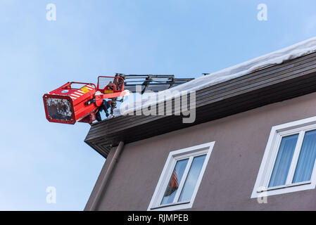 Mann in die teleskopantenne Plattform Reinigung Schnee und Eis von Dach, dachrinne der Gebäude die Gefahr zu vermeiden. Stockfoto
