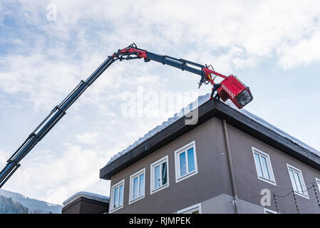 Mann in die teleskopantenne Plattform Reinigung Schnee und Eis von Dach, dachrinne der Gebäude die Gefahr zu vermeiden. Stockfoto