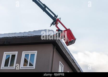 Mann in die teleskopantenne Plattform Reinigung Schnee und Eis von Dach, dachrinne der Gebäude die Gefahr zu vermeiden. Stockfoto