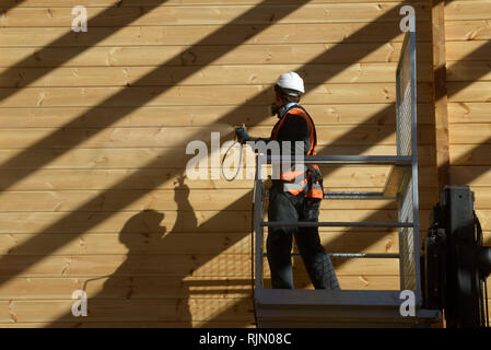 Handwerker Lackierung der Wand eines hölzernen Industriegebäude mit Holz Konservierungsmittel Stockfoto