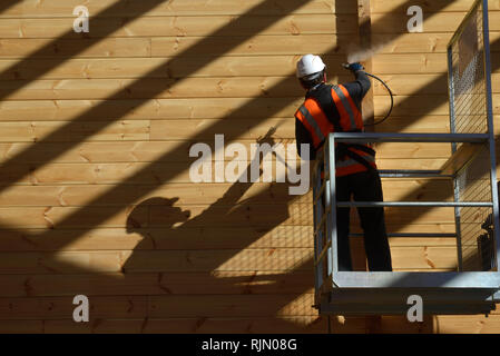 Handwerker Lackierung der Wand eines hölzernen Industriegebäude mit Holz Konservierungsmittel Stockfoto