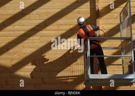 Handwerker Lackierung der Wand eines hölzernen Industriegebäude mit Holz Konservierungsmittel Stockfoto