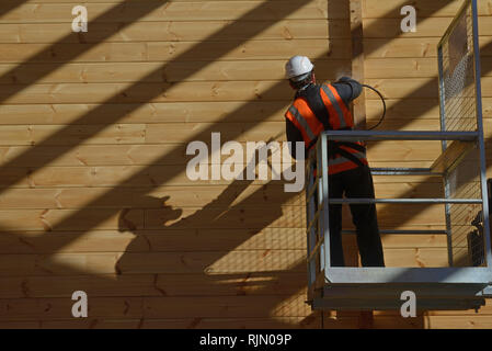 Handwerker Lackierung der Wand eines hölzernen Industriegebäude mit Holz Konservierungsmittel Stockfoto