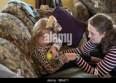 Ein 3 Jahre alter Kaukasische Mädchen Knuddel und spielt mit einem Kätzchen und ein Ball während einer erwachsenen Frau auf aussieht. Stockfoto