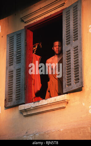 Bildunterschrift: Luang Prabang, Laos - Sep 2002. Eine junge Novizin blickt aus dem Fenster seines Zimmers im Wat Nong Sukhumerang in Luang Prabang. Stark influ Stockfoto