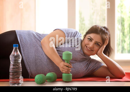 Lächelnd übergewichtige Frau auf dem Boden liegen und will sich nicht Übung Stockfoto