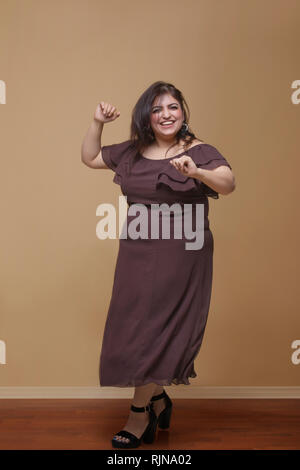 Fette Frau in einem langen braunen Kleid tanzen auf High Heels Stockfoto