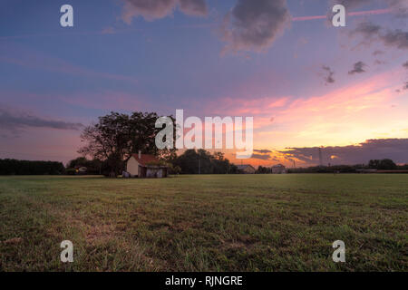 Isoloated Haus in das Feld bei Sonnenuntergang mit bewölktem Himmel Stockfoto