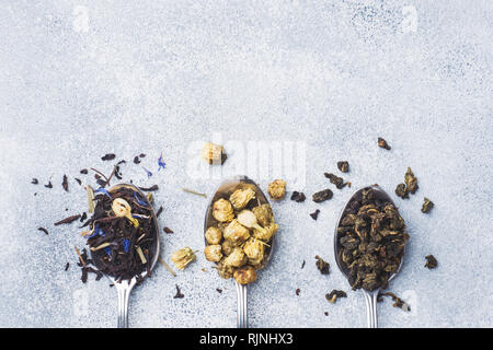 Vielzahl von trockenen Teeblätter und Blumen in den Löffel auf grauem Hintergrund. Stockfoto