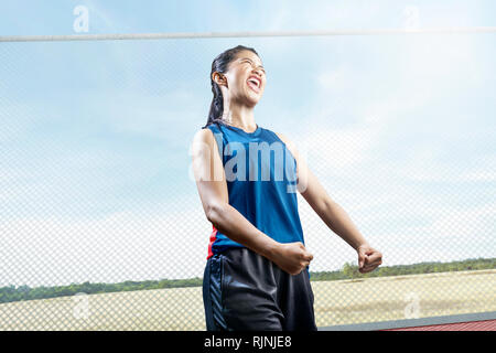 Junge asiatische Frau in Sportkleidung mit glücklichen Ausdruck auf der Outdoor Basketball Court Stockfoto