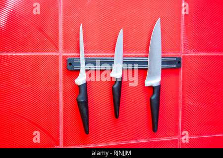 Qualitativ hochwertige Küche kochen Messer Werkzeuge auf einer Magnettafel hängen an der Roten Wand Stockfoto