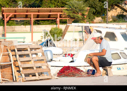 Insel Prvic, Kroatien - 23. August 2018: Fischer Instandsetzung seiner Fischernetz auf Pier mit Booten im Hintergrund Stockfoto