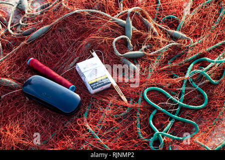 Insel Prvic, Kroatien - 23. August 2018: Fischer" Zubehör, rot Fischernetz mit Einwebung Nadel, Brillen, Zigaretten auf dem Pier in Sun Stockfoto