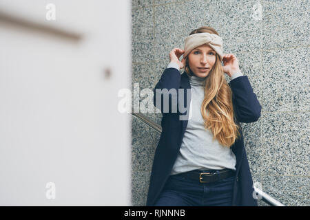 Schöne junge Frau auf einen Bügel auf der Treppe vor einer grauen Wand Stockfoto