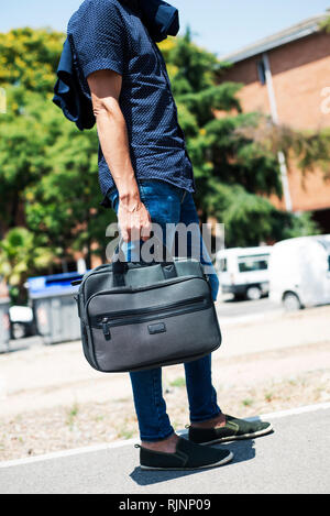 Nahaufnahme eines jungen kaukasischen Mann mit einem modernen Smart Casual Look, mit slim Jeans und Hemd, untucked seine Jacke hängen in einer Schulter, und Carr Stockfoto