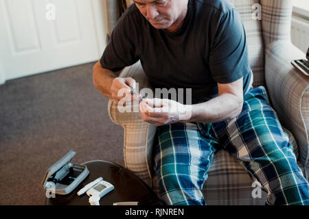 Ältere Diabetiker Mann bereitet sein Insulin pen im Wohnzimmer seines Hauses. Stockfoto