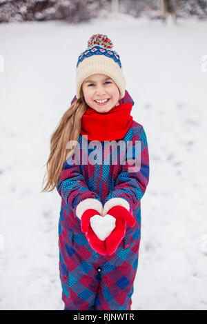 Ein Mädchen in roten Handschuhe hält eine herzförmige Schneeball. Symbol der Liebe zum Valentinstag. Stockfoto