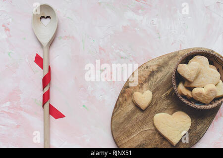 Rühren, Löffel und eine Schüssel mit Herzförmigen butter Cookies auf einem rosa Hintergrund. Frühlingsferien kochen und feiern. Ansicht von oben, flach, c Stockfoto