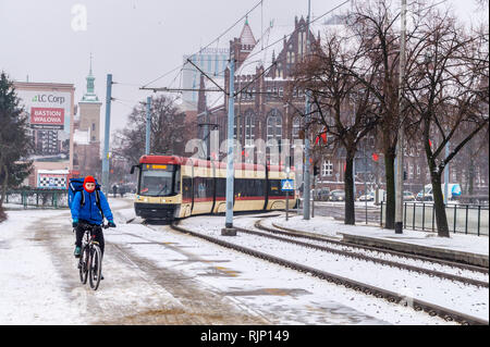 Ein Mann auf einem Fahrrad mit Straßenbahn nähert sich in Schnee, Plac Solidarnisci, Danzig, Polen Stockfoto