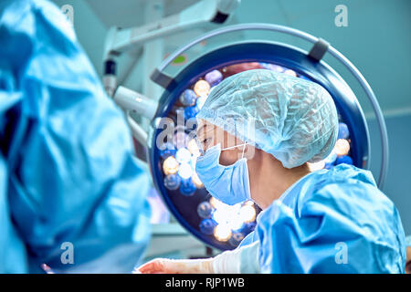 Close up Portrait von jungen weiblichen Chirurg Arzt durch das Tragen von schützender Maske und Hut während der Operation. Gesundheitswesen, medizinische Ausbildung, Chirurgie Konzept Stockfoto