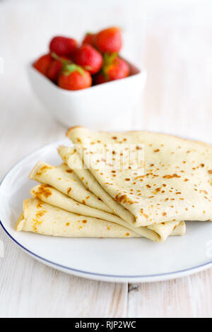 Crepes mit frischen Erdbeeren auf einem weißen Porzellanteller. Weiße Holztisch, hohe Auflösung Stockfoto