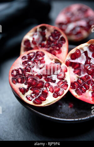 Reifen schneiden Granatapfel auf einer Schiefertafel Platte. Rote und dunkle Farben Zusammensetzung Stockfoto