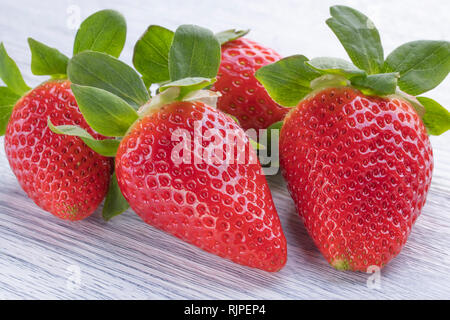 Vier Reifen saftigen Erdbeeren auf einem weißen Holz Hintergrund. Makro Stockfoto