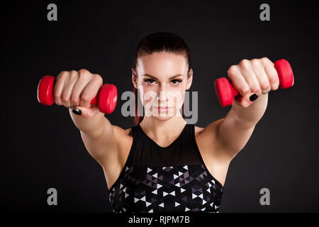 Schöne junge Frau Übungen mit Hanteln. Foto athletische Frau mit perfekten Körper auf schwarzem Hintergrund. Kraft und Motivation Stockfoto