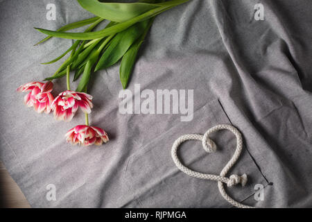 Herzen von Seil und Blumenstrauß aus Tulpen auf grauem Hintergrund mit Platz für Text Stockfoto