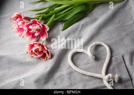 Herzen von Seil und Blumenstrauß aus Tulpen auf grauem Hintergrund mit Platz für Text Stockfoto