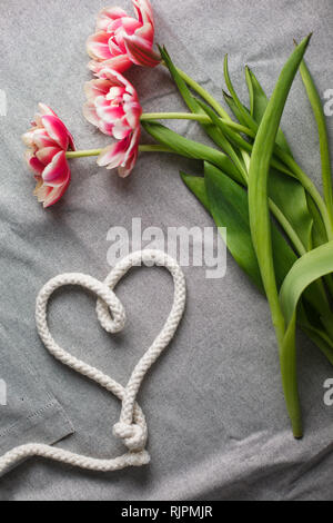 Herzen von Seil und Blumenstrauß aus Tulpen auf grauem Hintergrund mit Platz für Text Stockfoto