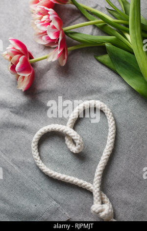 Herzen von Seil und Blumenstrauß aus Tulpen auf grauem Hintergrund mit Platz für Text Stockfoto