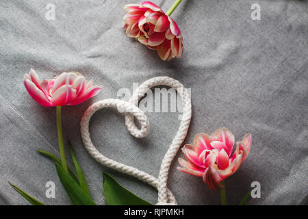 Herzen von Seil und Blumenstrauß aus Tulpen auf grauem Hintergrund mit Platz für Text Stockfoto