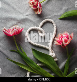 Herzen von Seil und Blumenstrauß aus Tulpen auf grauem Hintergrund mit Platz für Text Stockfoto