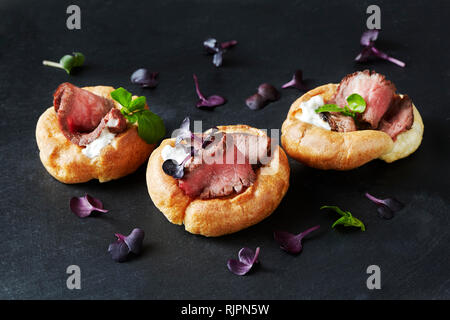 Stillleben mit Canapes Roastbeef in Yorkshire Pudding auf schwarzem Schiefer Stockfoto