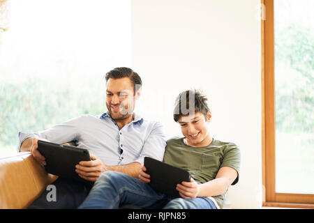 Sohn und Vater auf der Suche nach digitalen Tabletten während liegend auf Sofa Stockfoto