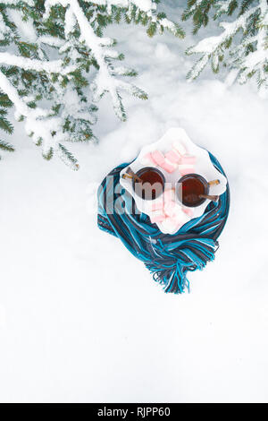 Zwei Tassen Tee mit Marshmallows unter einem Baum, in einer blauen Schal in den Schnee im Winter gewickelt Stockfoto