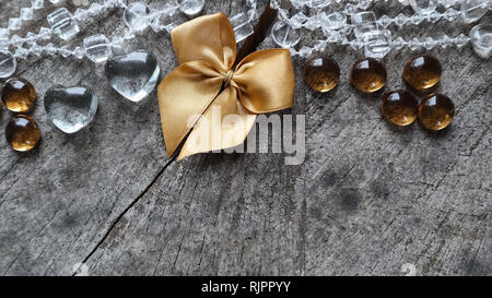 Glänzend goldenen Bogen, transparente Herzen und Perlen auf den rauen Hintergrund ein alter Baumstumpf mit einer Gaumenspalte Stockfoto