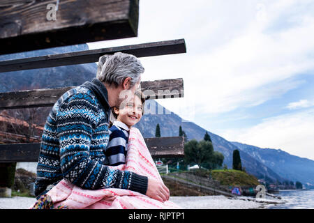 Junge und Vater aufgewickelt in der Decke auf See pier, Seitenansicht, Comer See, Onno, Lombardei, Italien Stockfoto