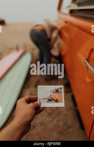 Junge Frau mit Instant Foto von Freund entfernen Reifenpanne auf recreational vehicle am Strand, Jalama, Kalifornien, USA Stockfoto