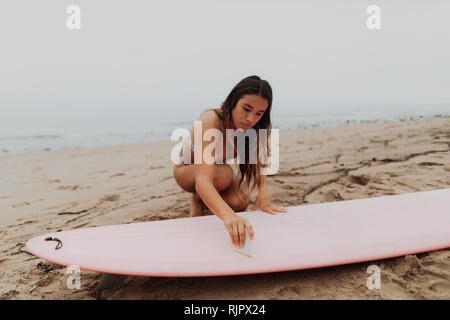 Junge weibliche Surfer waxing Surfboard am Strand, Ventura, Kalifornien, USA Stockfoto
